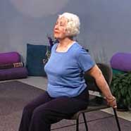woman in chair holds back of chair and stretches heart forward